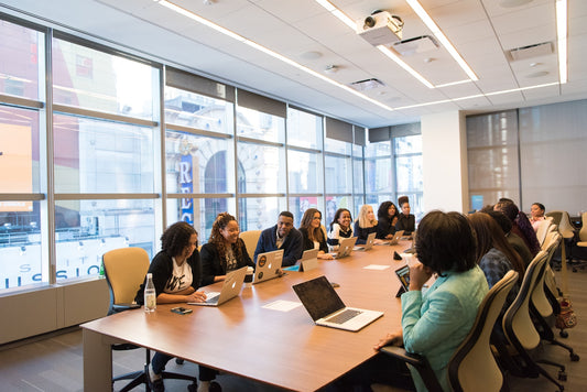 Office clothing banner image. People wearing office clothing around a table talking.