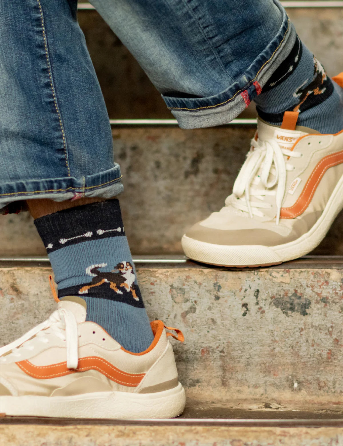 Person wearing blue socks with dog design and white sneakers with orange accents on a metal surface.