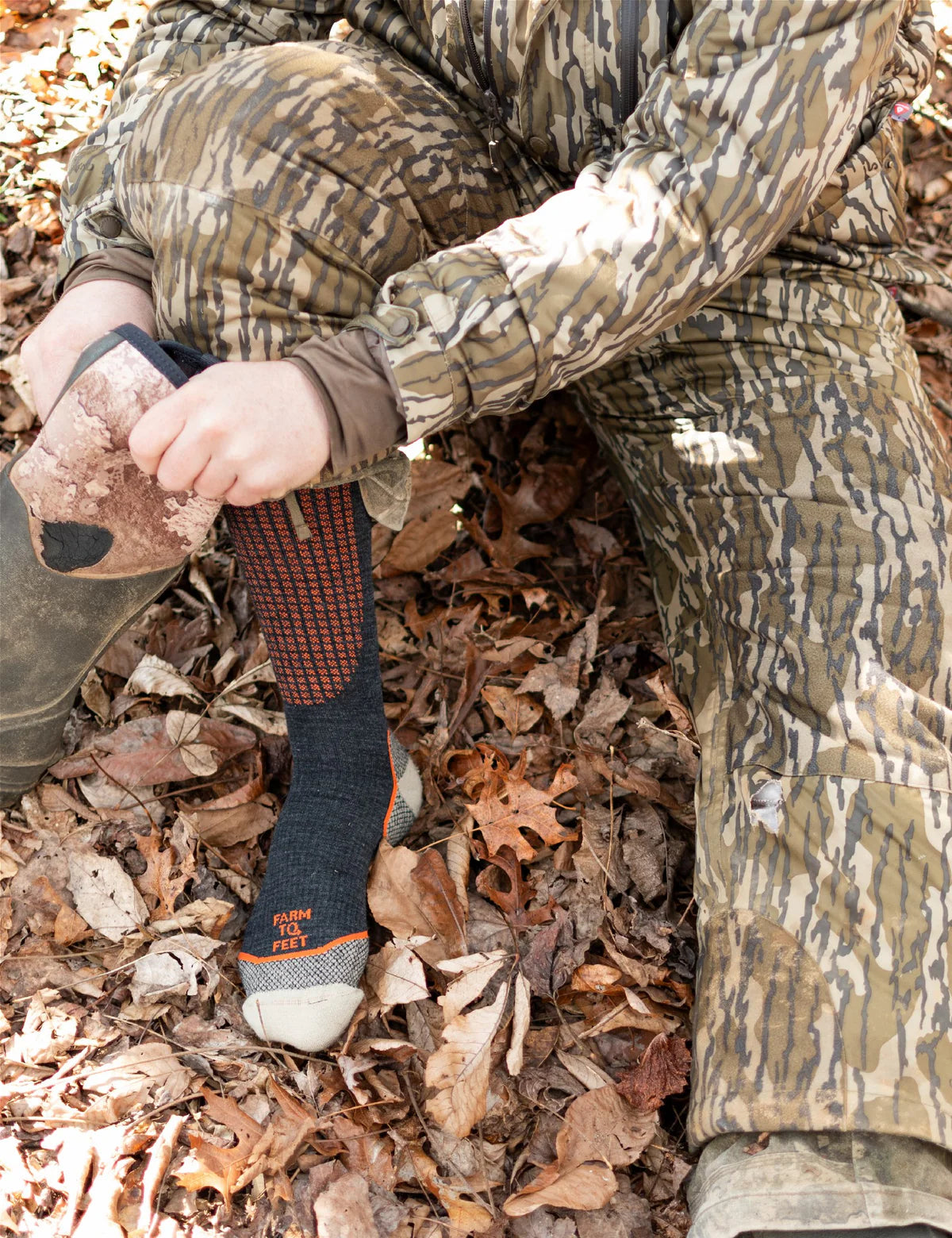 Person in camouflage clothing and socks sitting on a pile of leaves