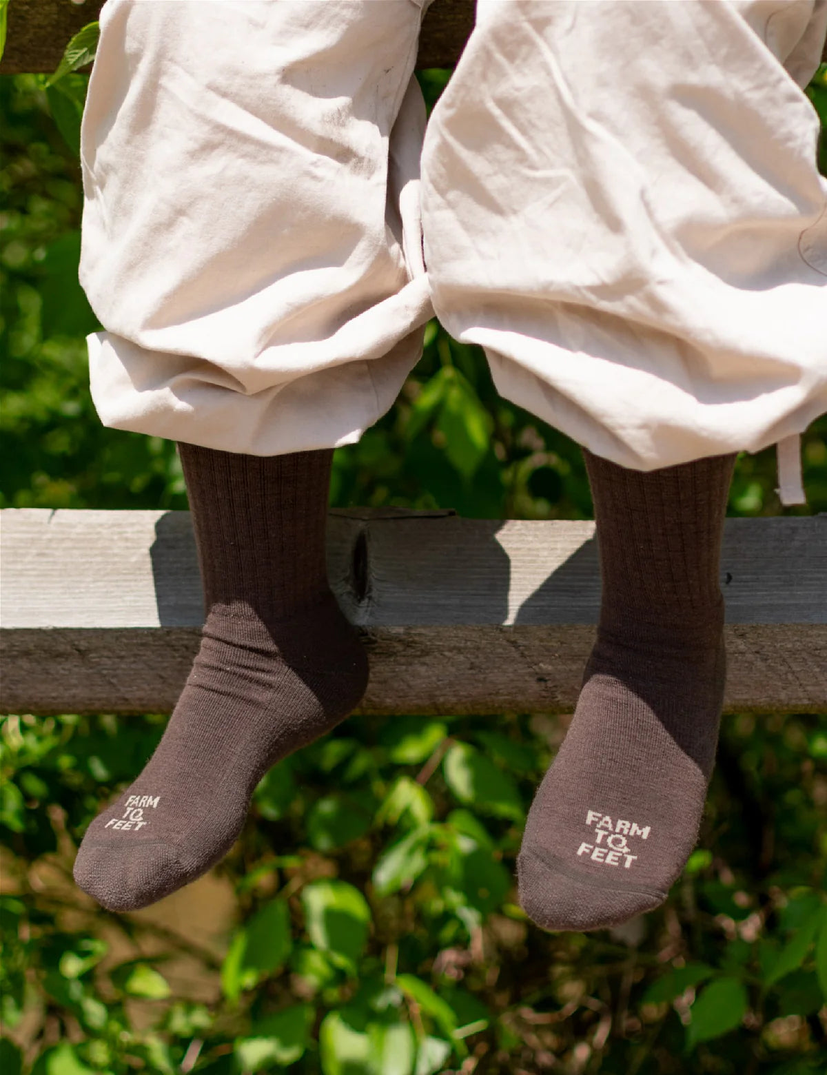 Person wearing brown socks with text, sitting on a wooden fence with a natural background