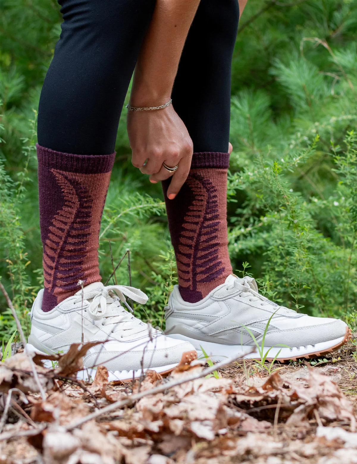 Person wearing maroon knee-high socks with a leaf pattern, standing in a forest.