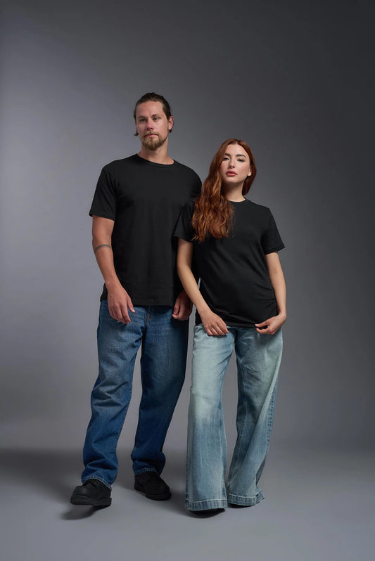 Two people wearing black t-shirts and blue jeans standing against a gray background