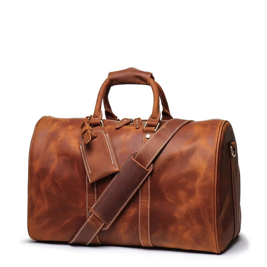 Small brown leather duffle bag with top handles, crossbody strap, and side zipper pocket