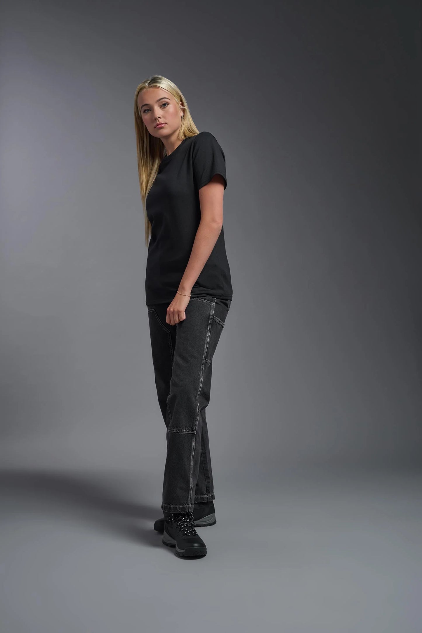 Person wearing a black t-shirt and dark jeans against a gray background