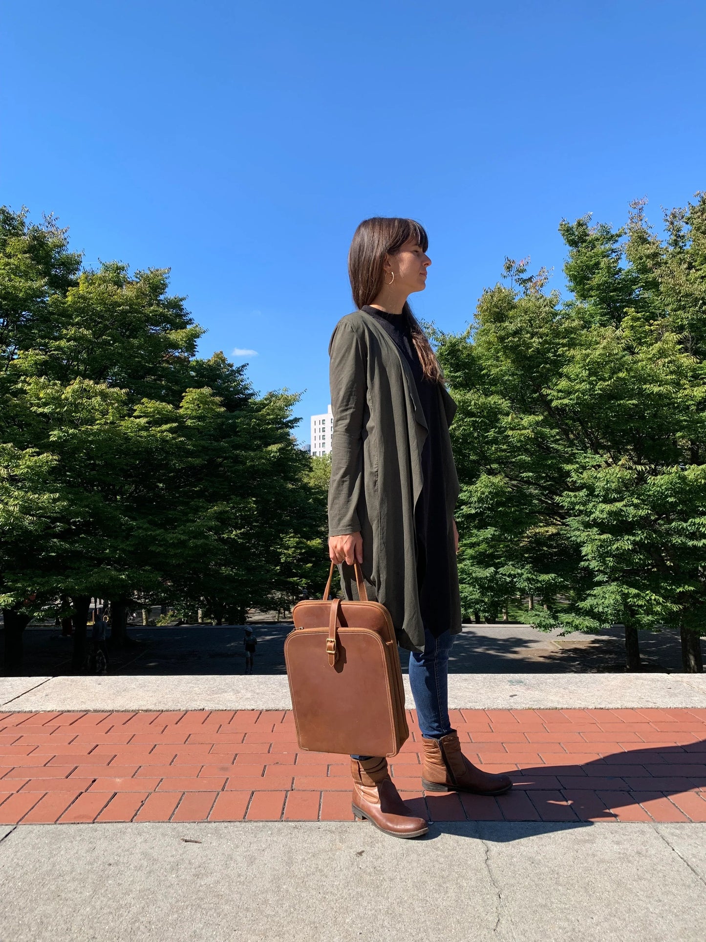 Small brown leather backpack with top handle and front pocket, worn crossbody.
