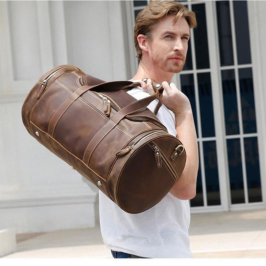 Brown leather weekender duffel bag with long shoulder strap and multiple front zip compartments.