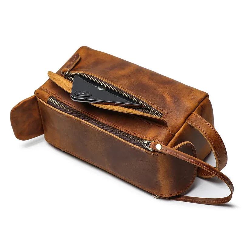 Brown leather toiletry bag with zip opening, front pocket, and adjustable shoulder strap.