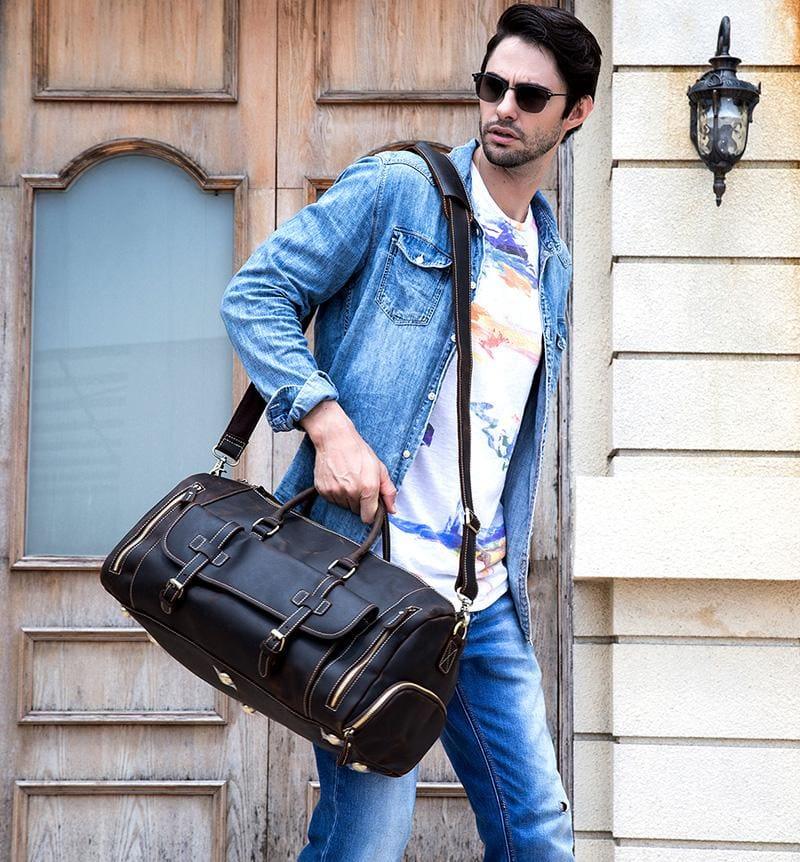 Dark brown leather duffle bag carried by shoulder strap with front buckles