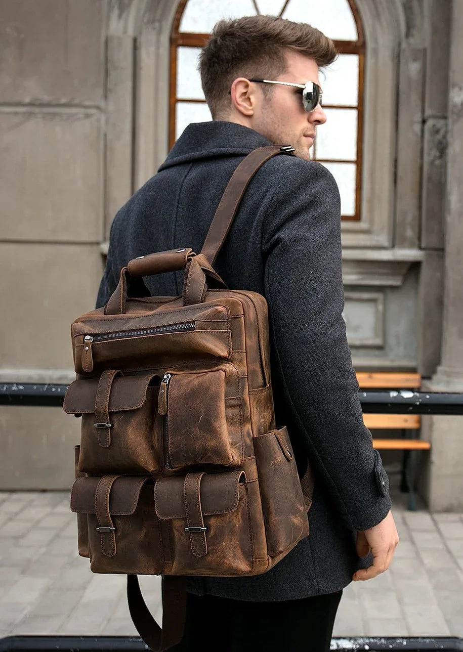 Brown leather backpack worn on shoulders with front zip and flap pockets.