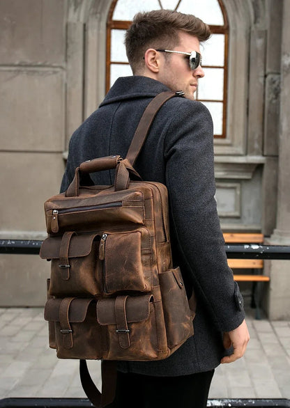 Brown leather backpack worn on shoulders with front zip and flap pockets.
