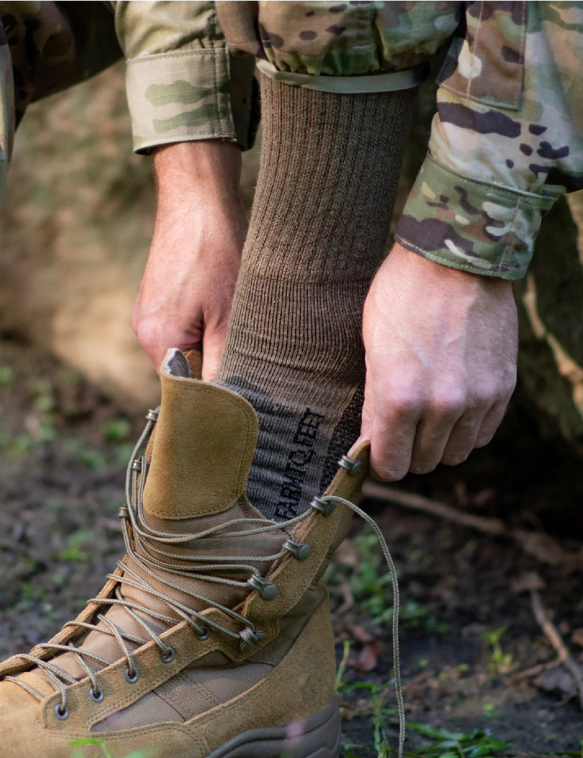 Person wearing camouflage clothing and brown socks with a boot outdoors.