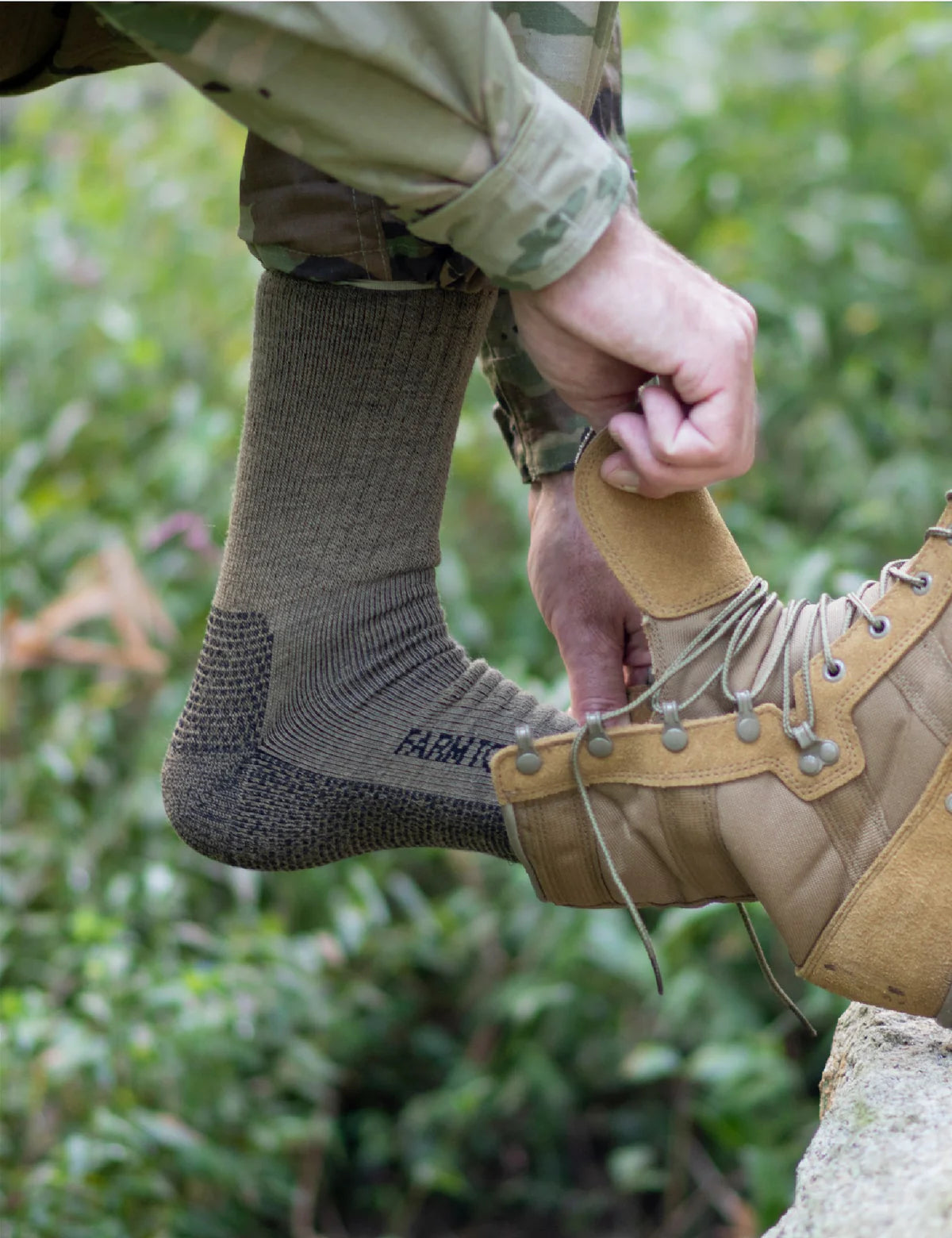Person wearing a tan boot and brown sock with a blurred green background