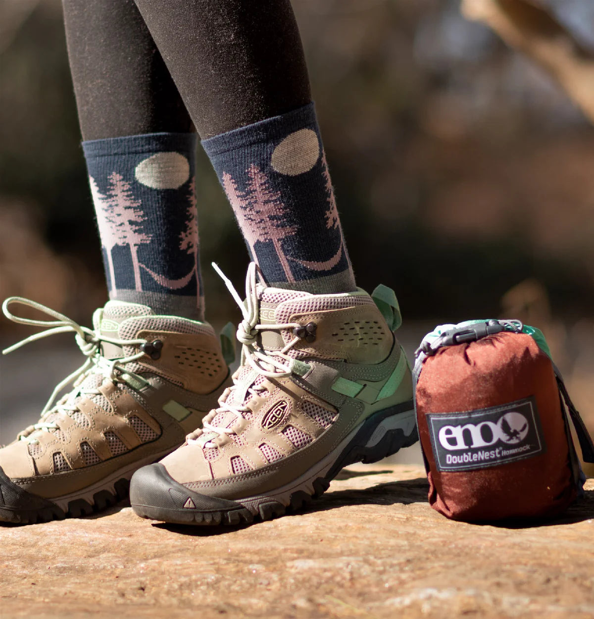 Person wearing hiking boots and socks with a nature design, next to a sleeping bag with 'ENO' branding.