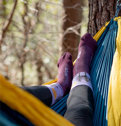 Person relaxing in a hammock with feet visible, surrounded by trees.
