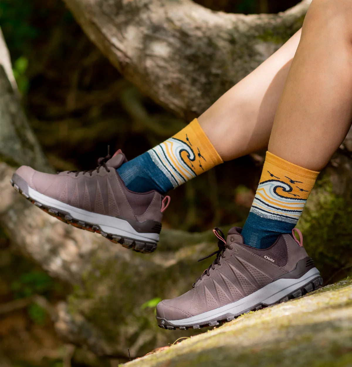 Person wearing brown hiking shoes and colorful socks with a nature-themed design.