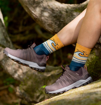 Person wearing brown hiking shoes and colorful socks with a nature-themed design.