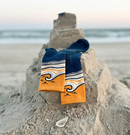Pair of blue and orange socks with wave design on a sandcastle at the beach.
