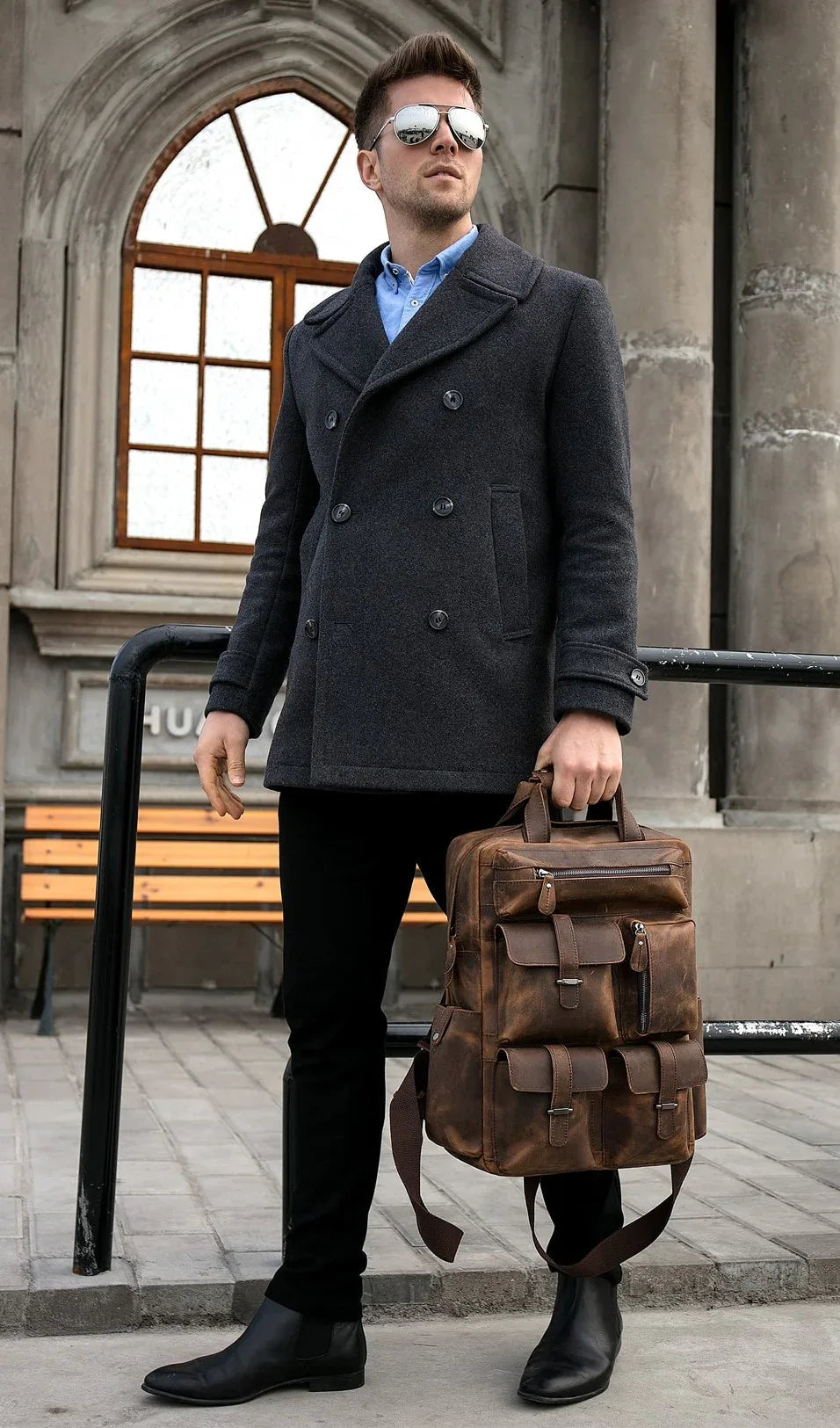Brown leather backpack with top handle and front flap pockets, carried in hand.
