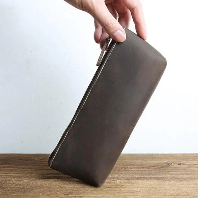 Brown leather pencil case held in hand with zip closure and stitched trim