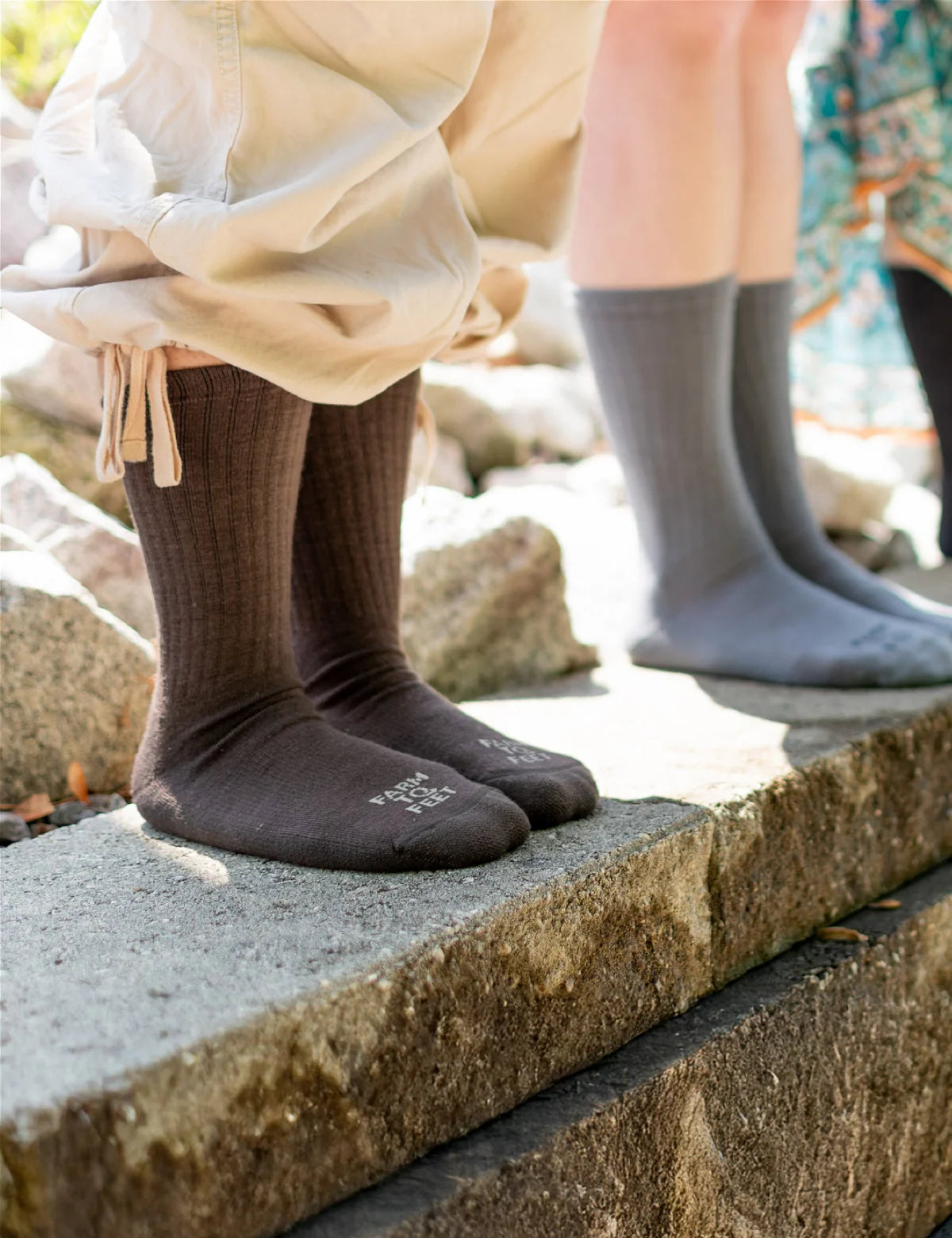 Two pairs of socks, one brown and one gray, worn by people standing on a stone ledge.
