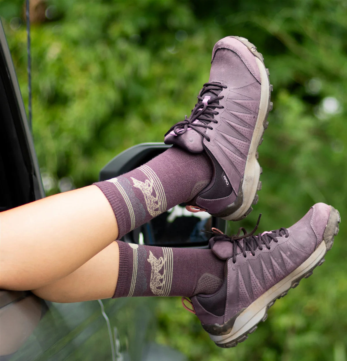 Purple hiking boots and socks with a blurred green background