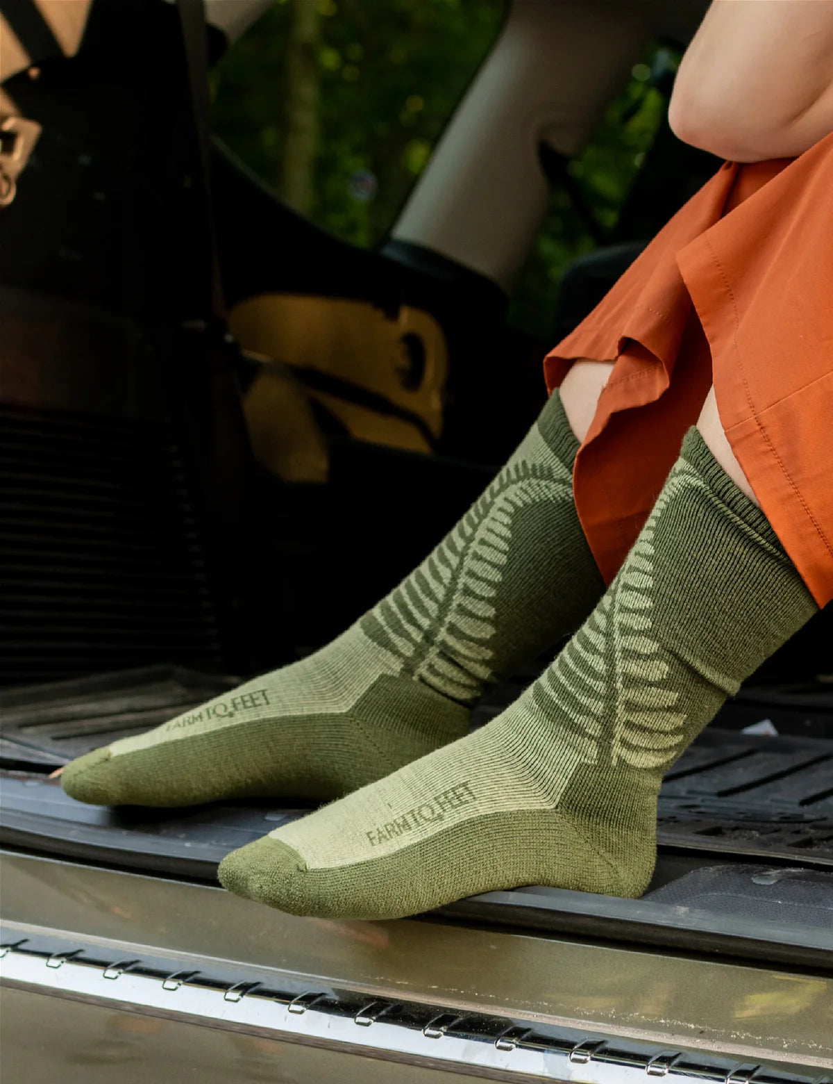 Person wearing green socks with a brand logo, standing on a vehicle bumper outdoors.