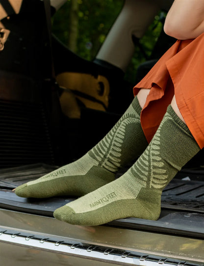 Person wearing green socks with a brand logo, standing on a vehicle bumper outdoors.