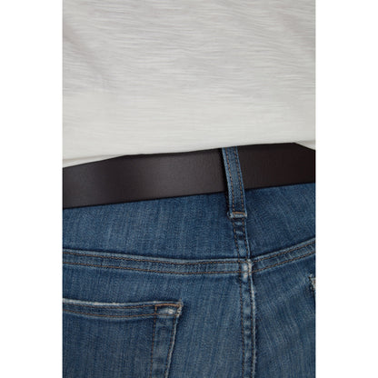 Close-up of a person wearing blue jeans with a black belt and a white shirt.