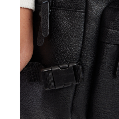 Close-up of a black leather backpack with a buckle detail.