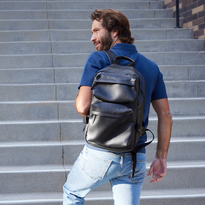 Man with a beard wearing a black leather backpack on a staircase.
