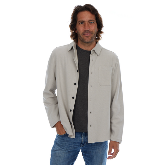 Man wearing a light gray jacket over a dark shirt and blue jeans on a white background