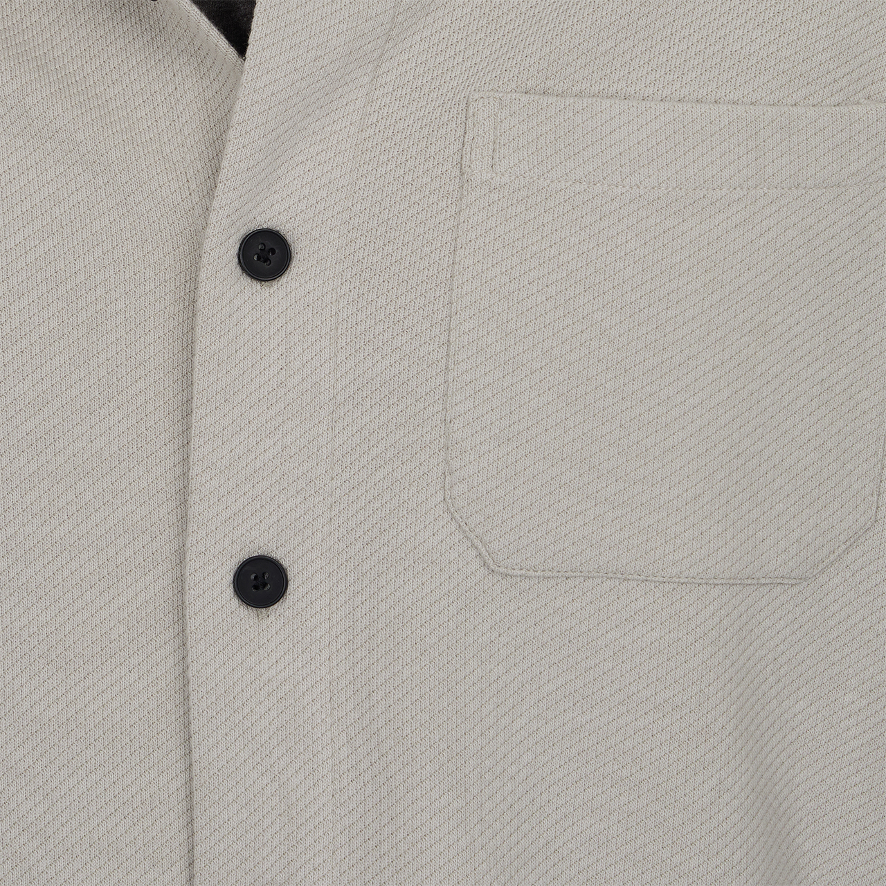 Close-up of a light gray jacket with black buttons and a pocket.