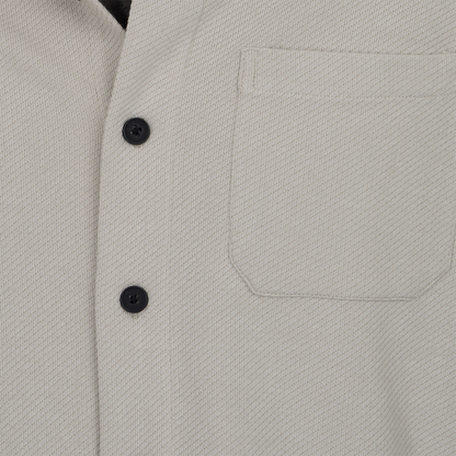 Close-up of a light gray jacket with black buttons and a pocket.