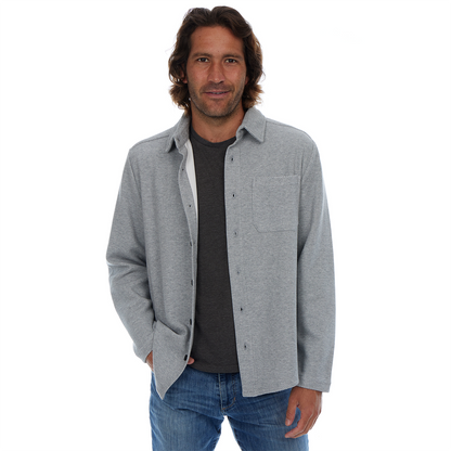 Man wearing a gray button-up shirt over a dark t-shirt with blue jeans on a white background