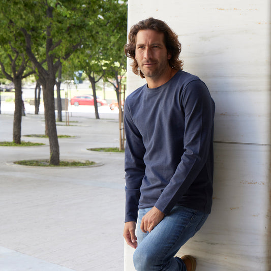 Man leaning against a wall outdoors with trees and cars in the background
