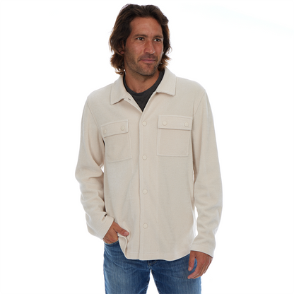 Man wearing a beige button-up shirt and blue jeans on a white background