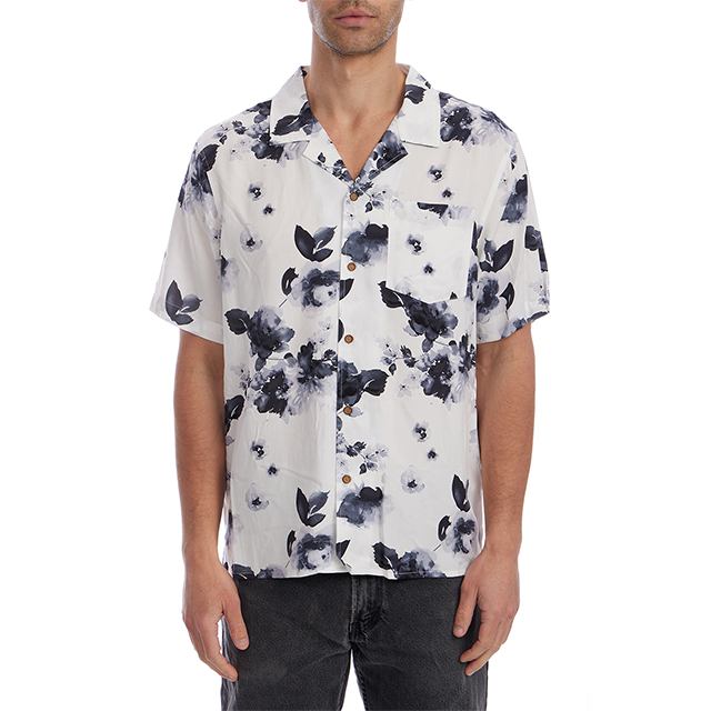 A man wearing a white short-sleeve button-up shirt with a dark navy watercolor floral print, paired with dark gray jeans, against a plain white background.