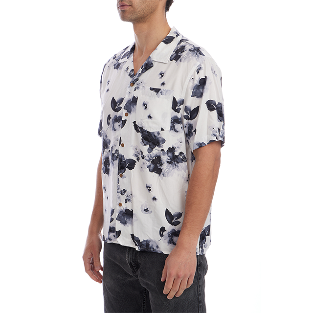 A man wearing a white short-sleeve button-up shirt with a dark navy floral watercolor print, paired with dark gray jeans, shown from the side against a plain white background.