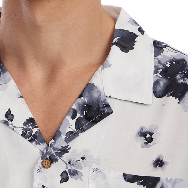 Close-up of a person wearing a white short-sleeve button-up shirt with a dark navy floral watercolor print and a brown button.