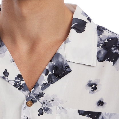Close-up of a person wearing a white short-sleeve button-up shirt with a dark navy floral watercolor print and a brown button.