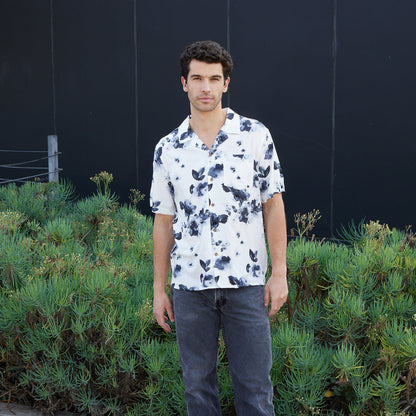 Man wearing a white floral shirt standing in front of greenery