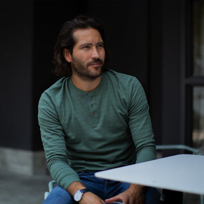 Olive Green Long Sleeve Henley for Men. Model sitting outside in public behind a table.