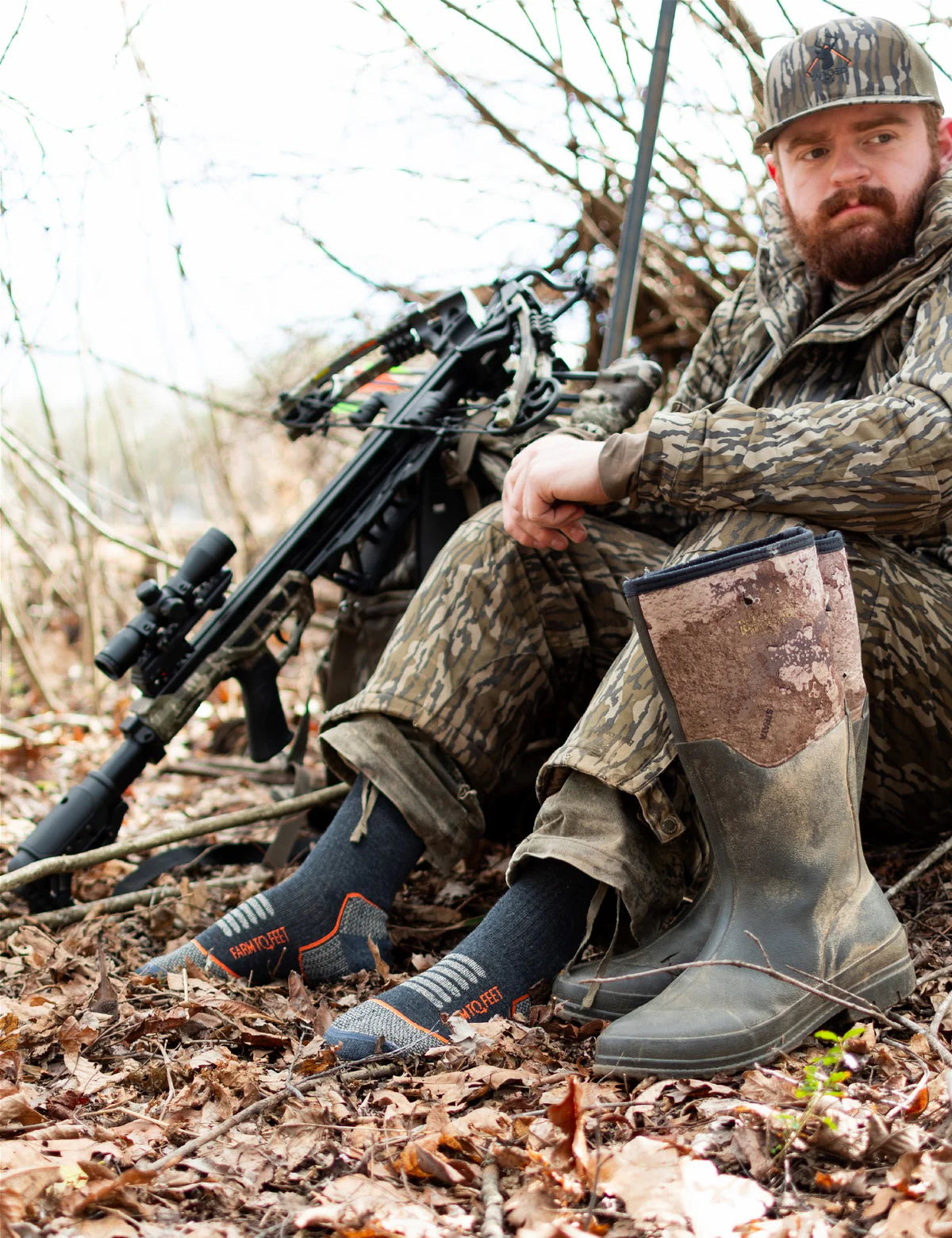 Hunter sitting in the woods with hunting gear, including a crossbow and camouflage clothing.