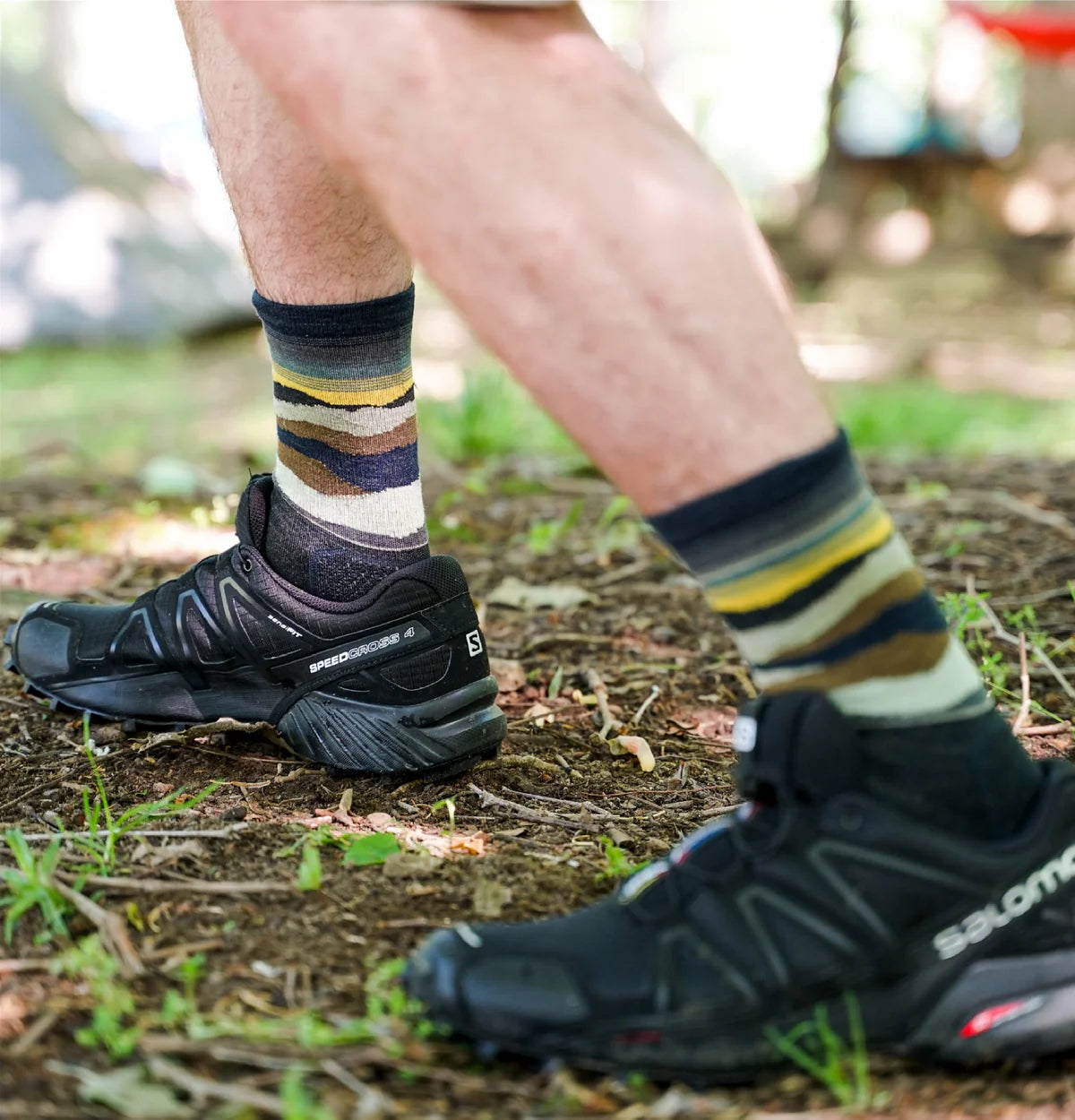 Person wearing black Salomon shoes and striped socks outdoors on a trail.