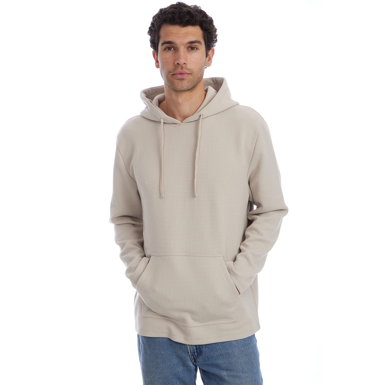 Man wearing a beige hoodie and blue jeans on a white background