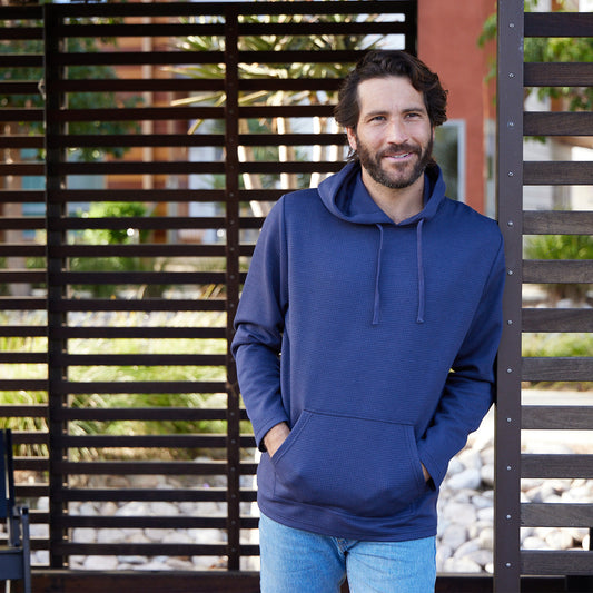 Man wearing a blue hoodie standing in front of a wooden fence.
