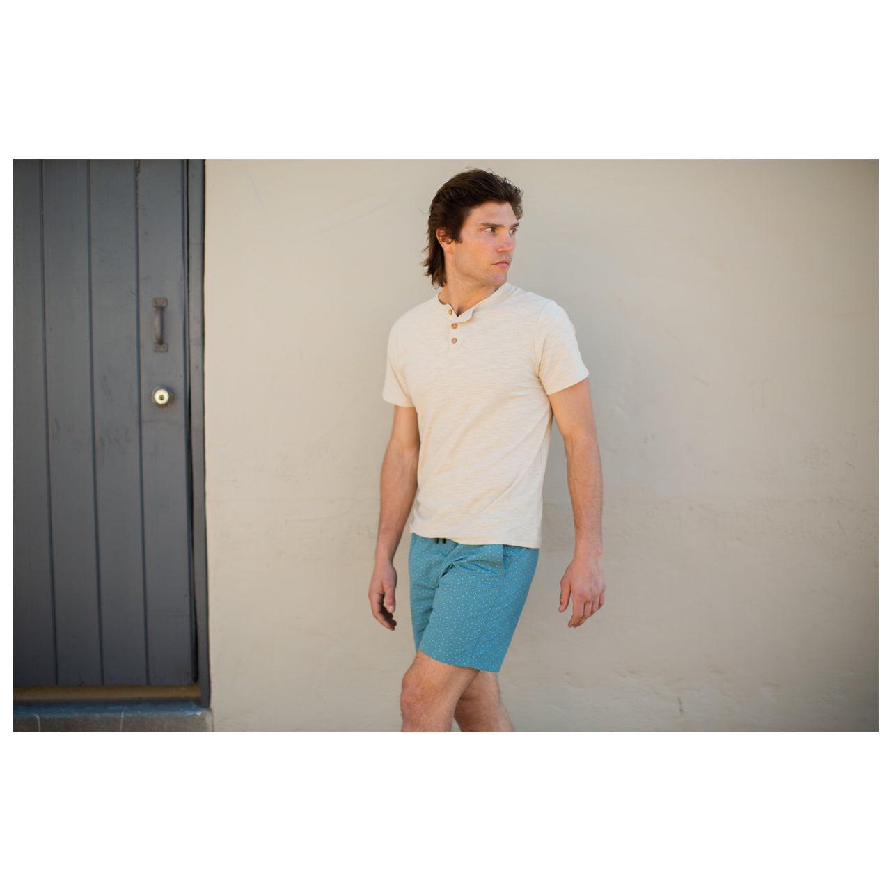 Plain Short Sleeve Sand Colored Henley for Men. Model standing in front of a wall outside.