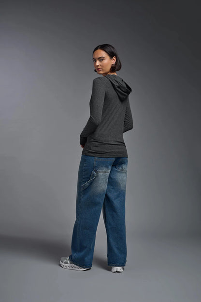 Person wearing a dark gray hoodie and blue jeans standing against a gray background