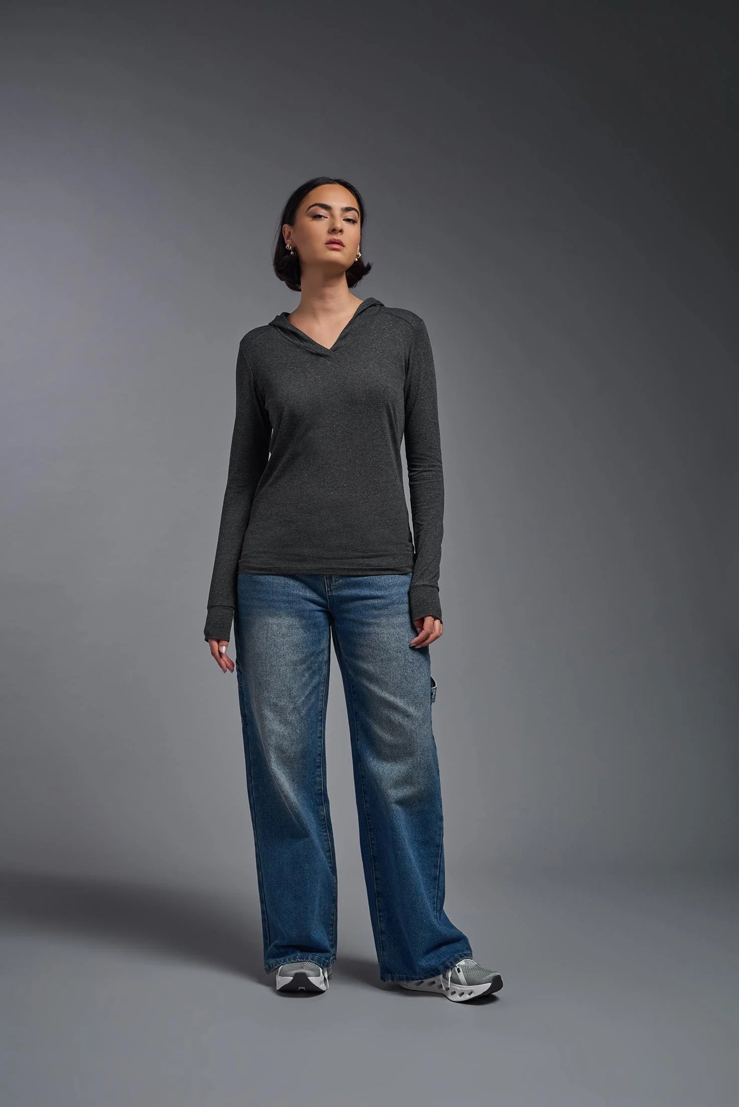 Person wearing a dark gray long-sleeve shirt and blue jeans against a gray background