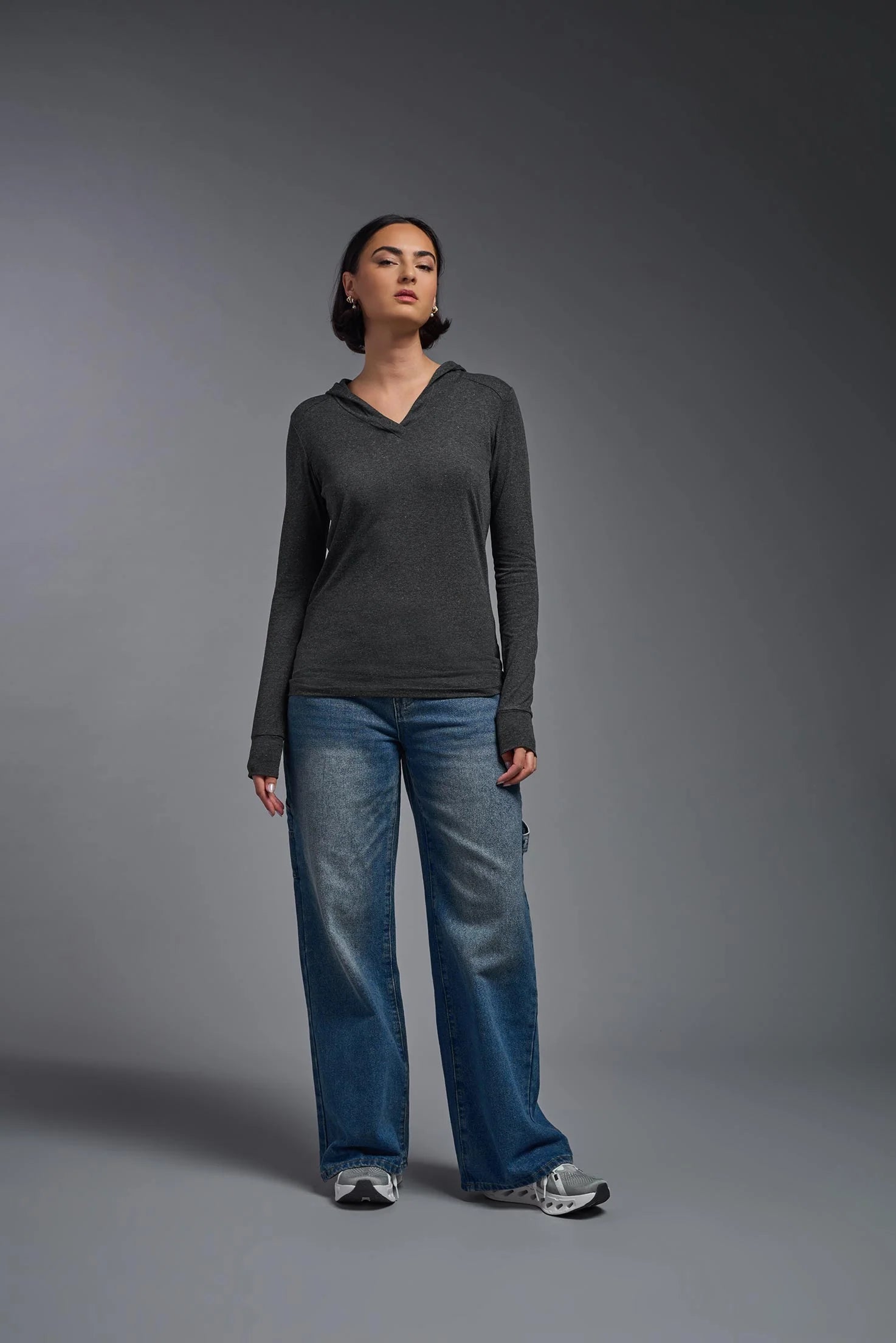 Person wearing a dark gray long-sleeve shirt and blue jeans against a gray background